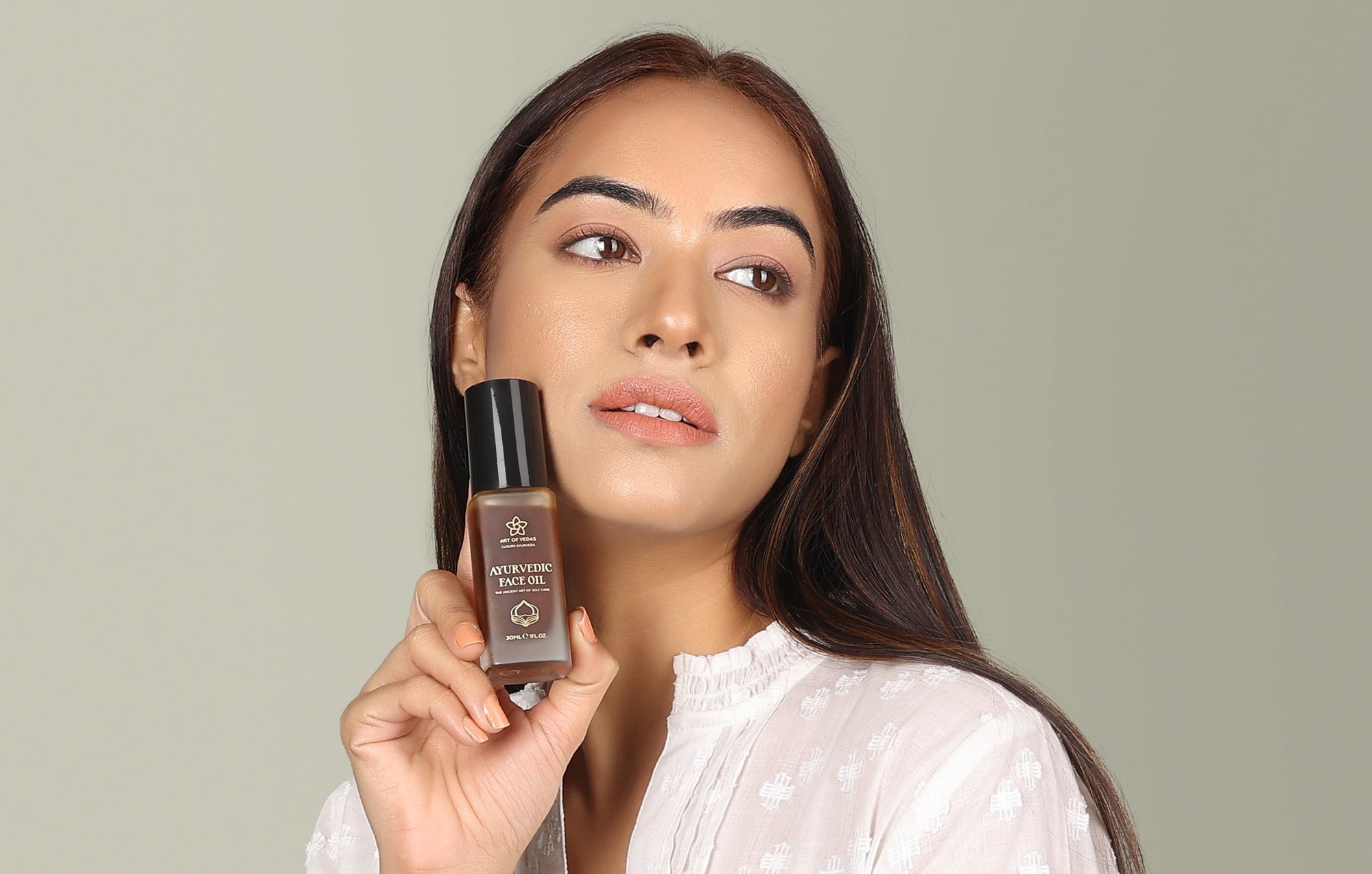 Woman holding a Art of Vedas Ayurvdic skincare bottle against a neutral background