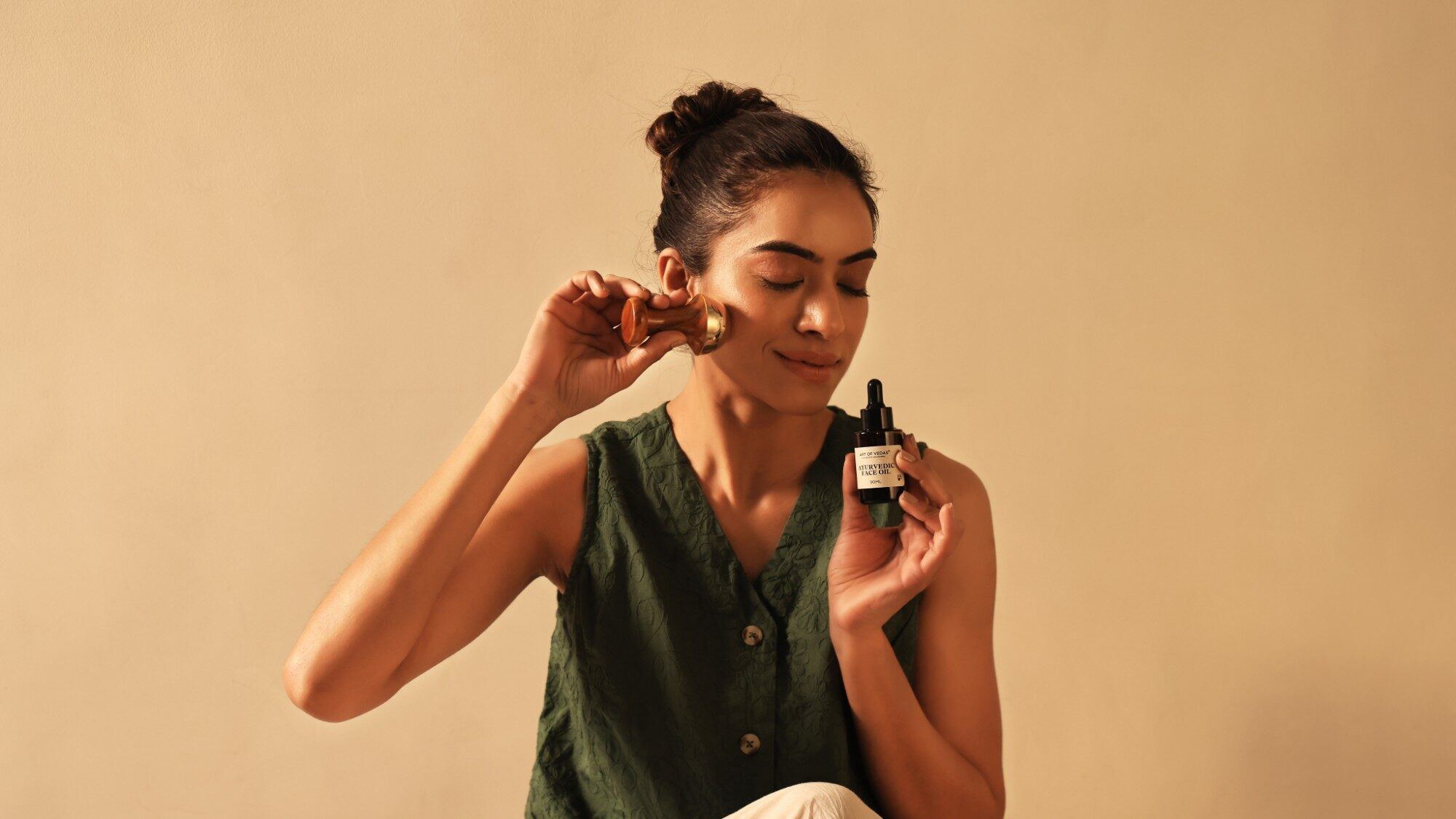 Vrouw gebruikt een Kansa gezichtswand op haar wang en houdt Art of Vedas Ayurvedische Gezichtsolie vast